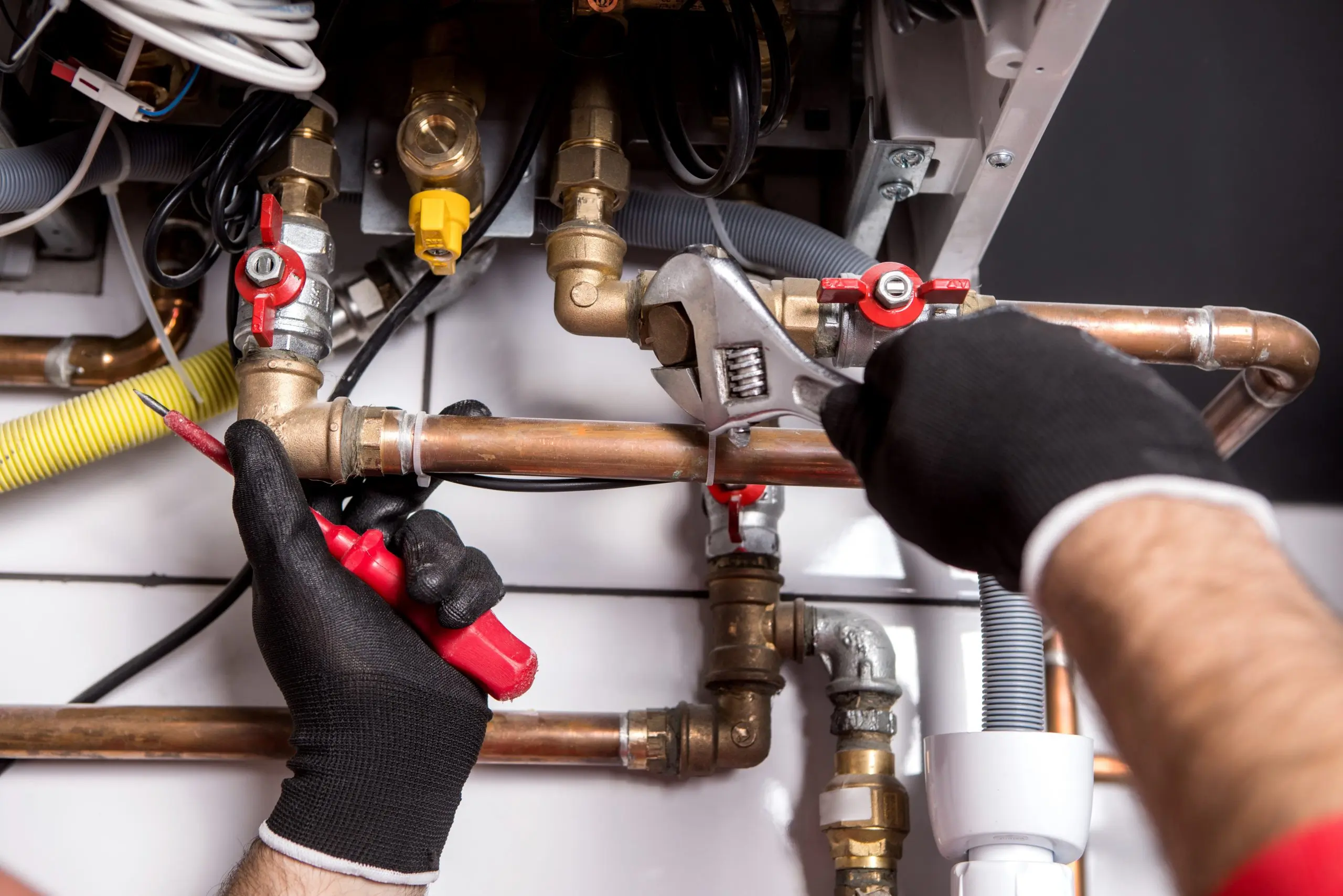 Gloved hands using a wrench on boiler pipework and valves