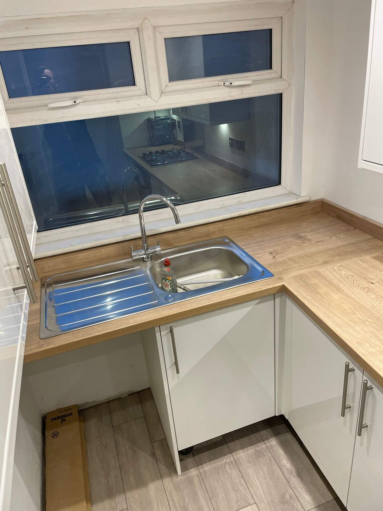 Stainless steel kitchen sink fitted beneath a window in a wood-effect worktop