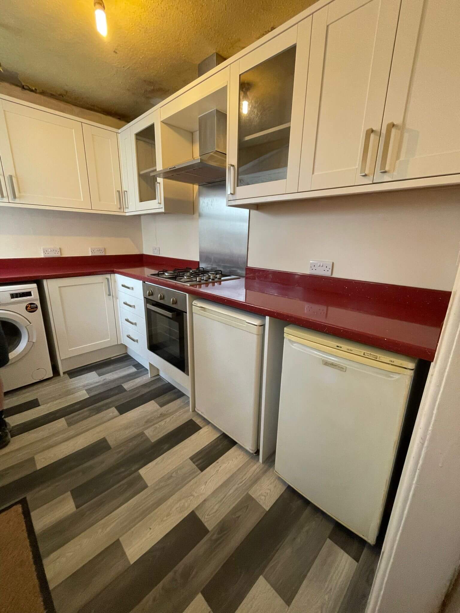 White fitted kitchen with red worktops, a gas hob and under-counter appliances