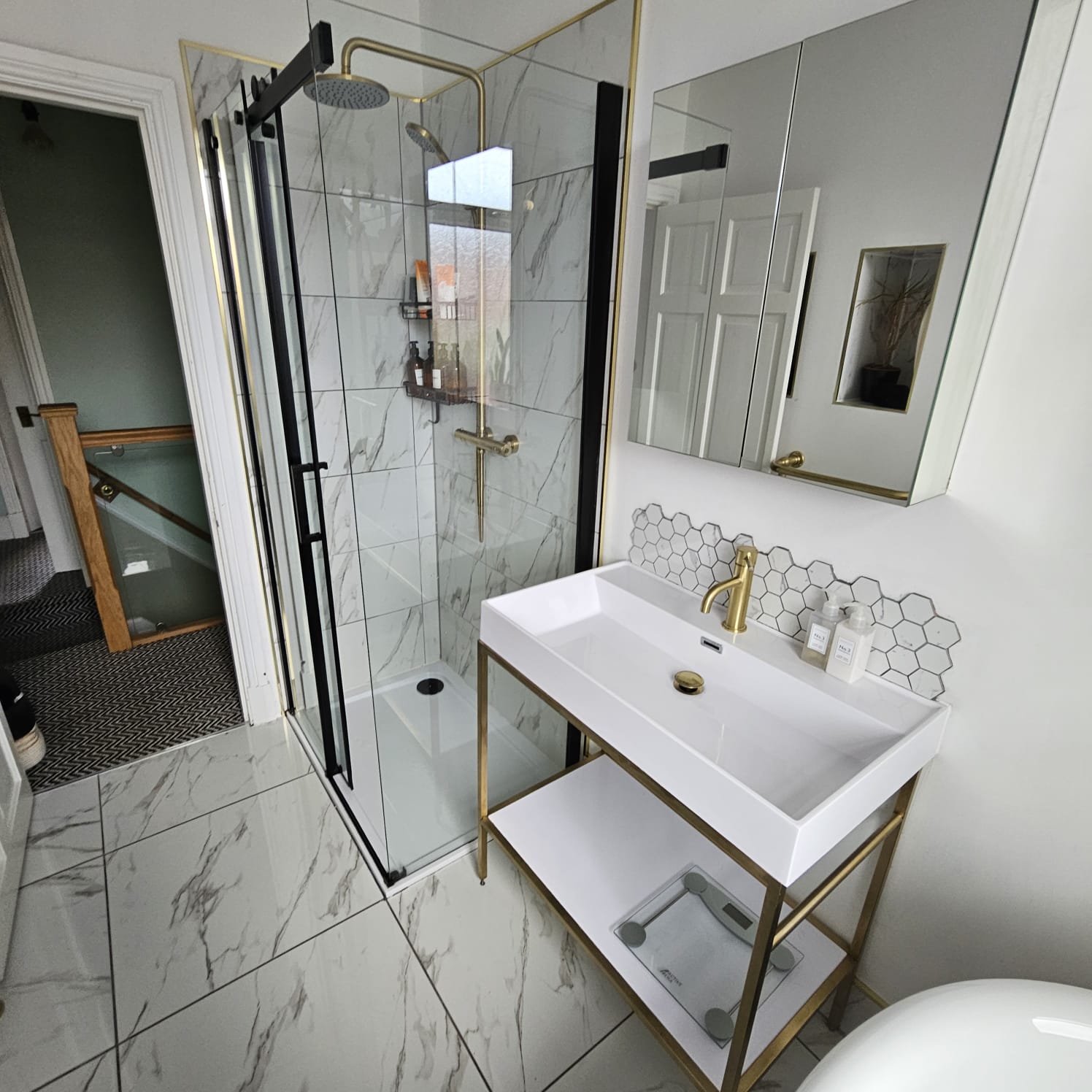 Bathroom with a glass shower enclosure, marble-effect tiles and a white basin with brass fittings