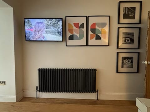Black column radiator fitted beneath framed pictures in a living room