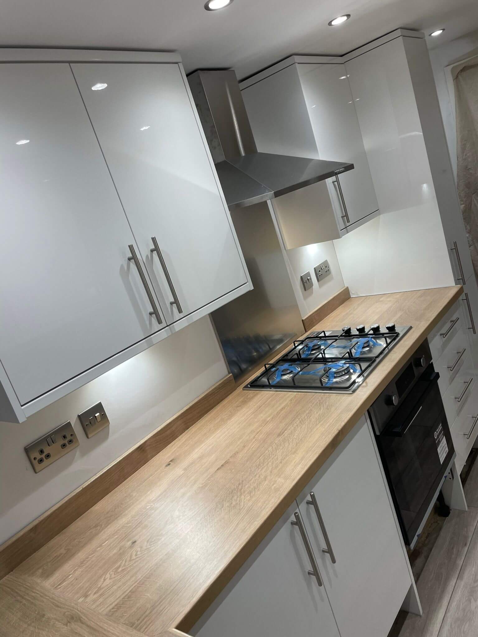 White fitted kitchen with wood-effect worktops, a gas hob and stainless steel extractor